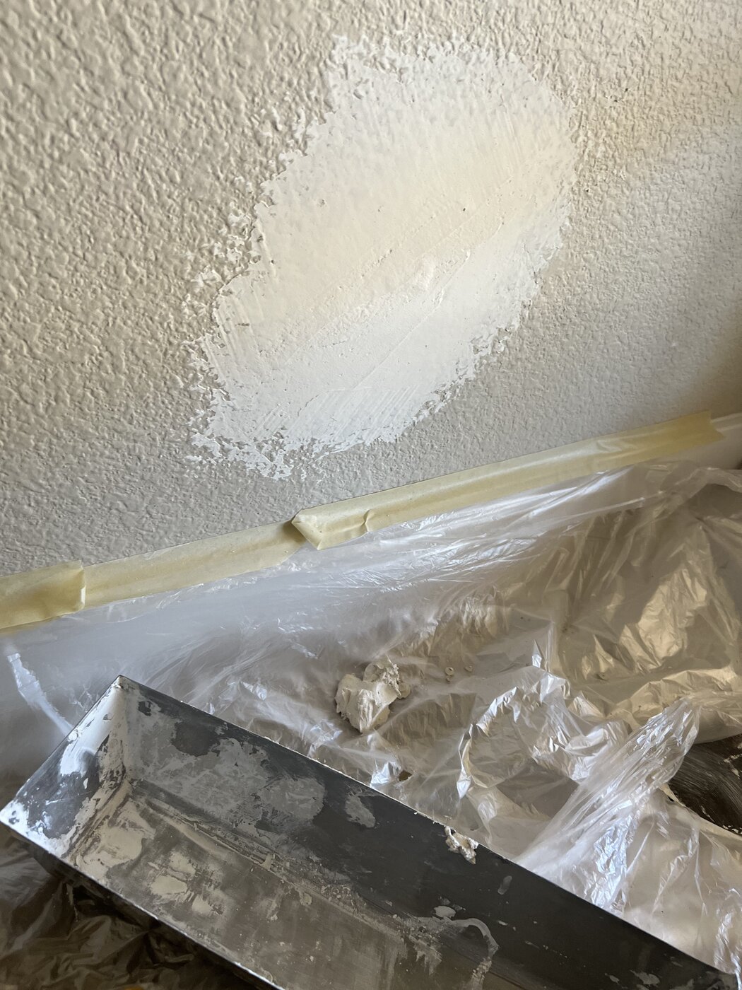 Wall with joint compound patch applied over a repaired hole, taped and masked off