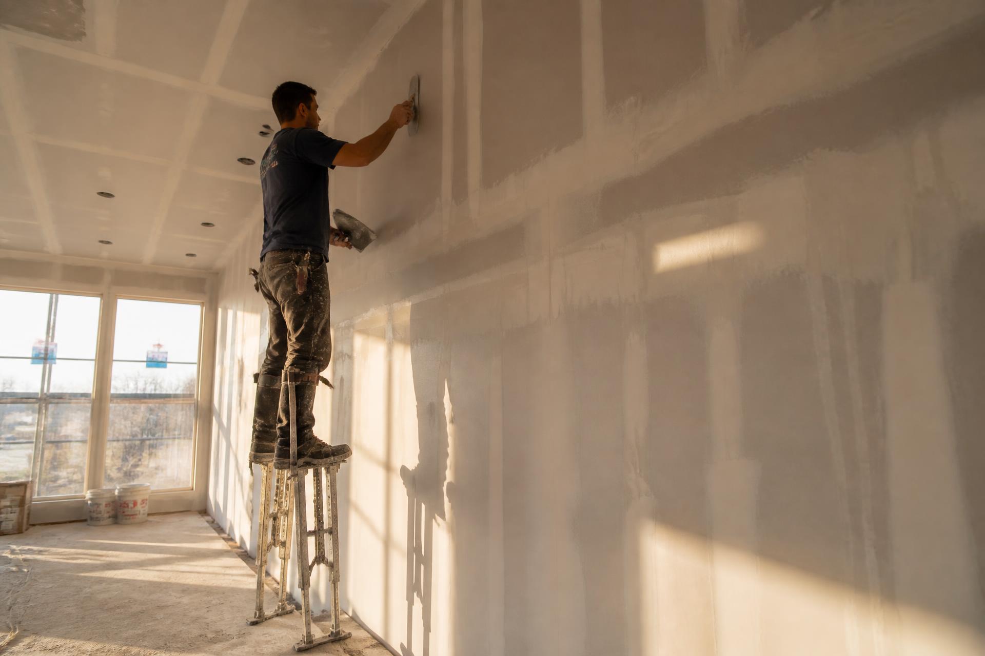 Drywall finisher on stilts smoothing joint compound on a new interior wall